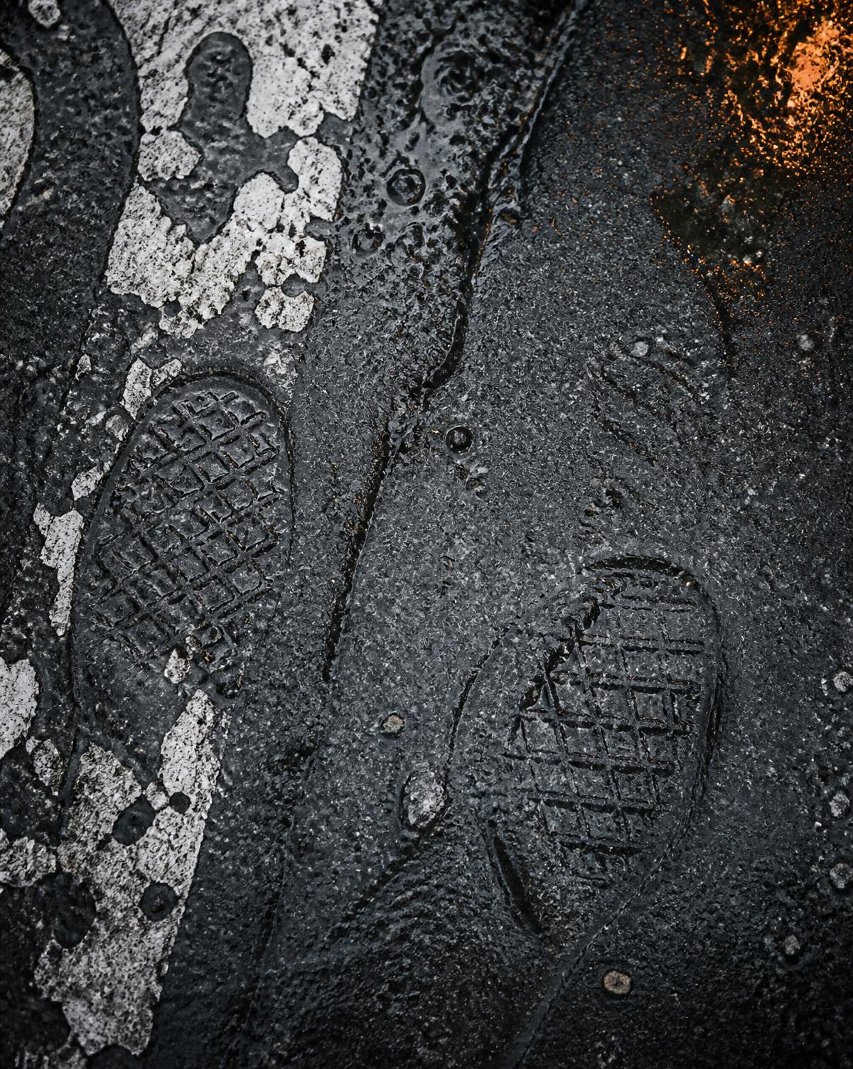 Close do asfalto úmido com pegadas de tênis e tinta branca descascada